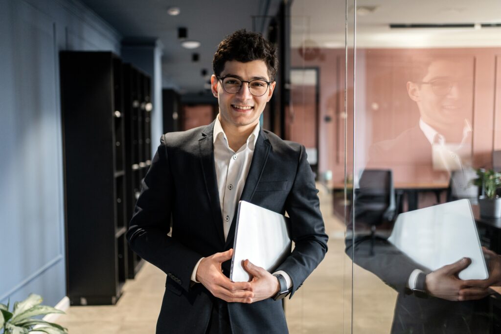 A young business professional standing and smiling in the hallway of an office.