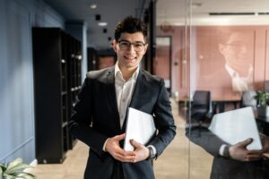 A young business professional standing and smiling in the hallway of an office.